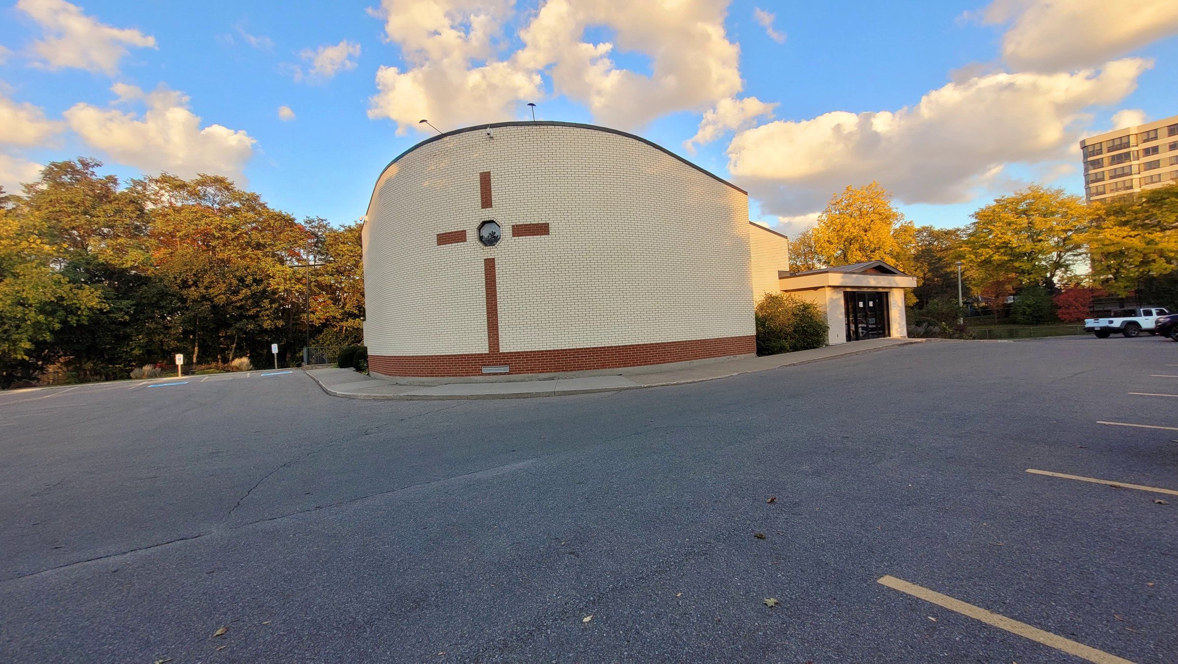 Augsburg Lutheran Church, a cream brick building with a curved roofline and a red-brick cross on its end wall, beyond its car park