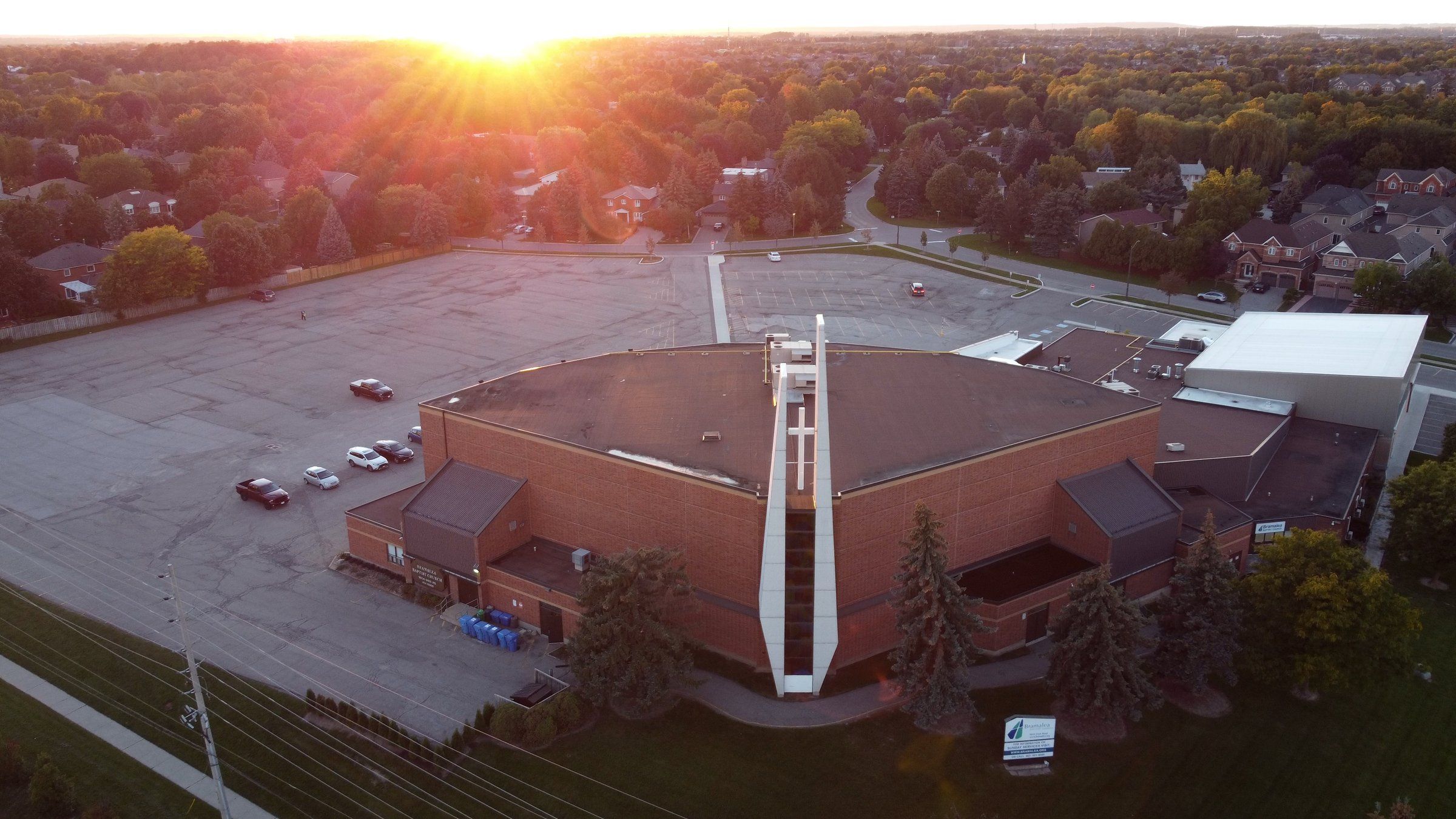 Bramalea Baptist Church from the air at sunset, a broad brick building with a tall white tower beside its car park