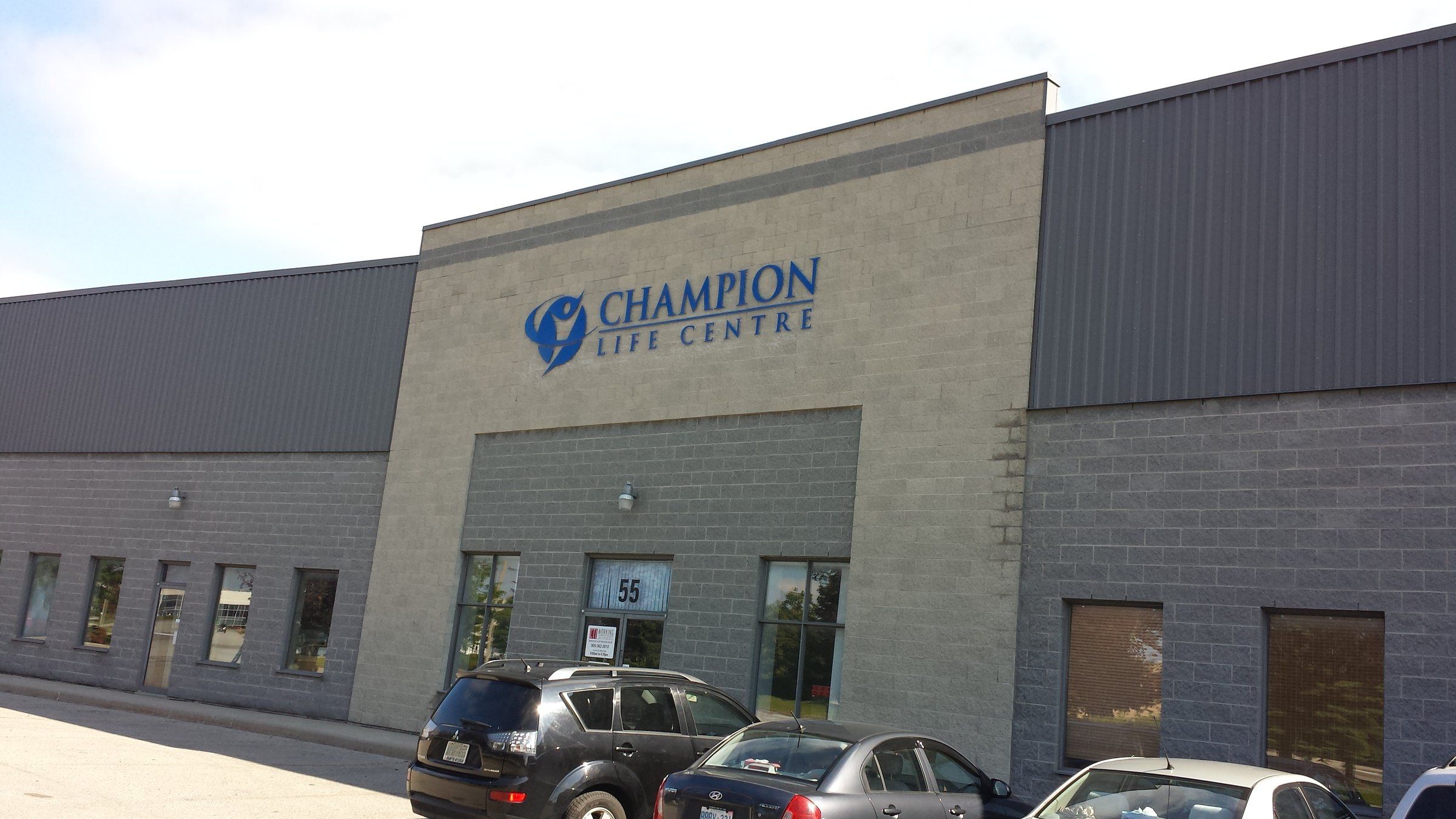 Champion Life Centre, a grey industrial building with the church's name on its front and cars parked outside
