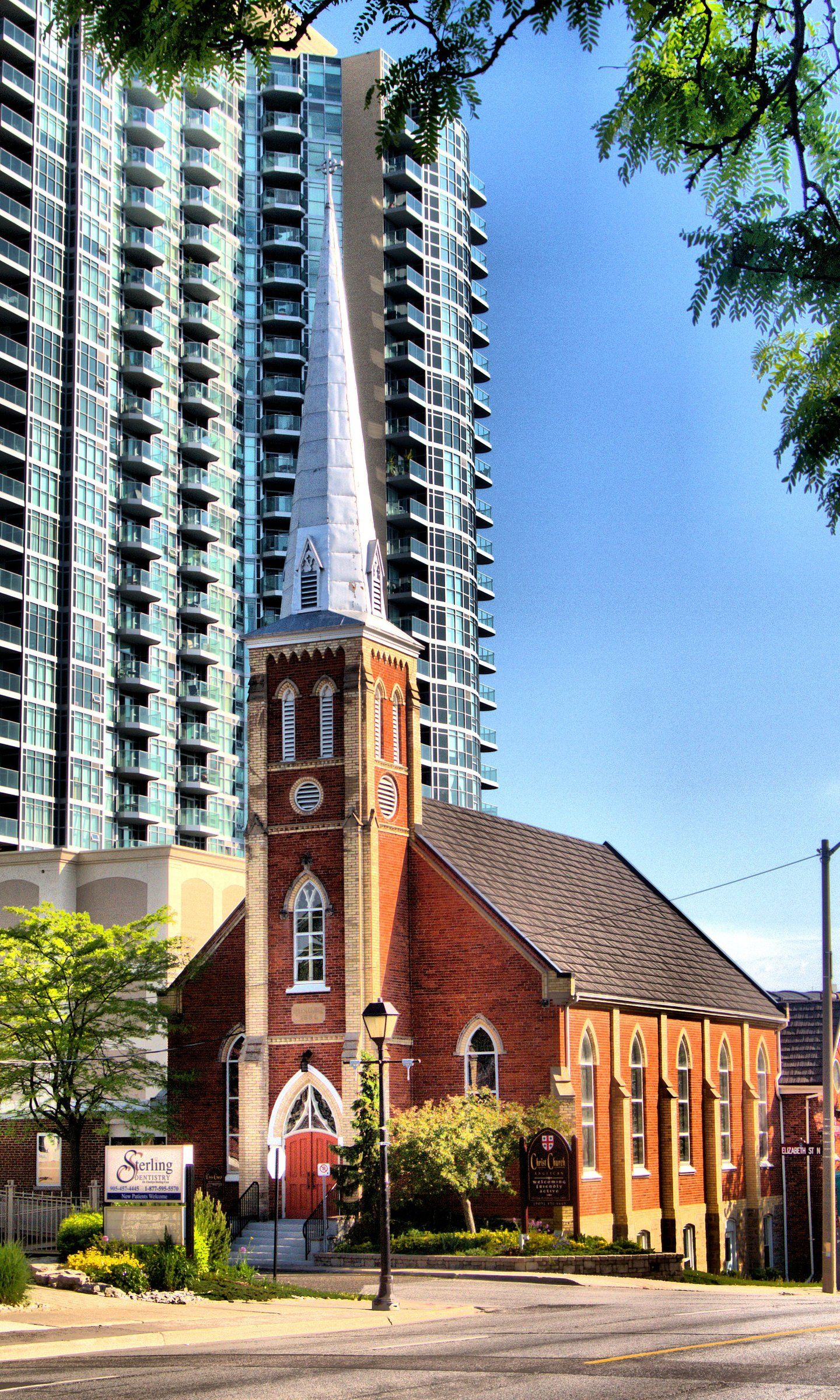 Christ Church, a red-brick church with buff-brick buttresses and a tall white spire, in front of a glass condominium tower