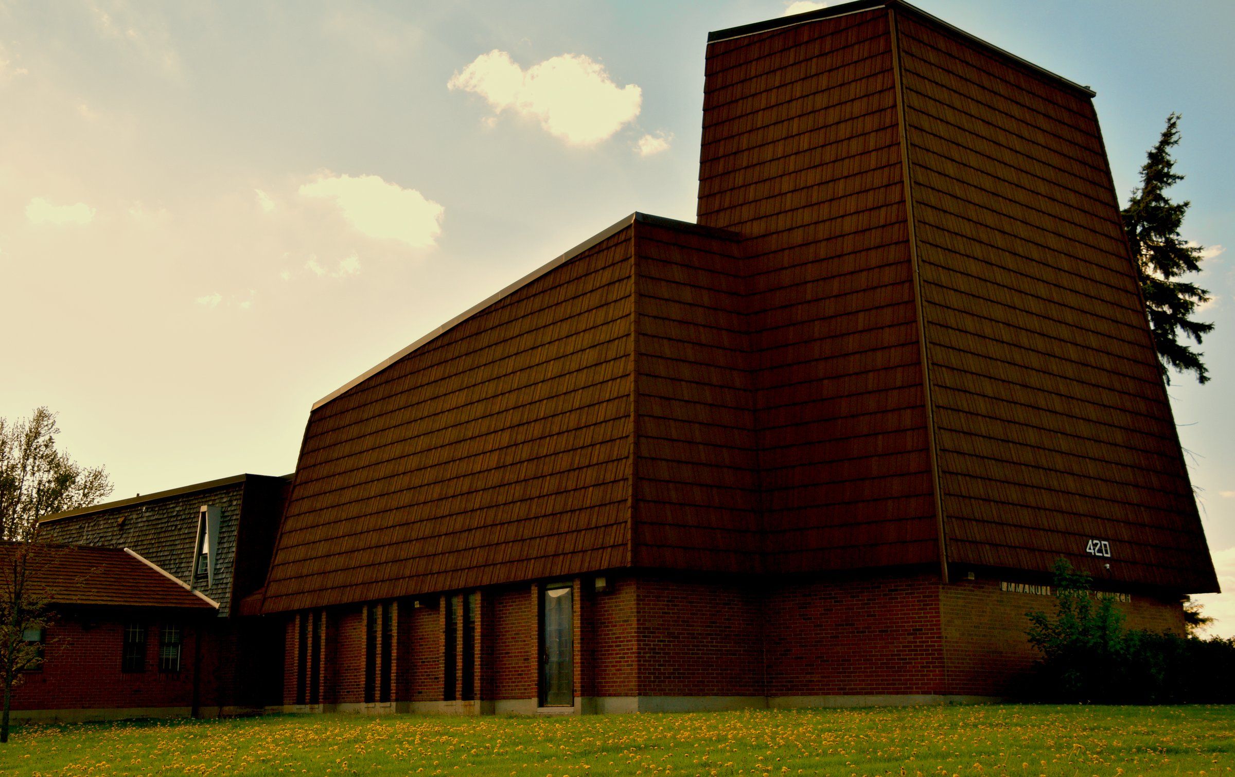 Emmanuel United Church, a tall angular tower clad in brown shingles above a brick base, in evening light