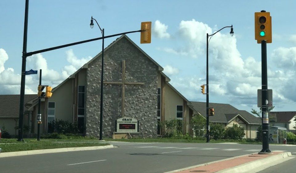 Grace Canadian Reformed Church, a stone-fronted church with a large cross on its gable and its sign before it, seen across the intersection of Creditview Road and Fairhill Avenue