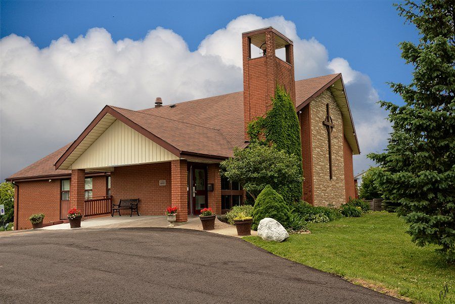 The Church of the Holy Family, a brick church with an open square bell tower and a stone wall marked with a cross, beside a curving driveway