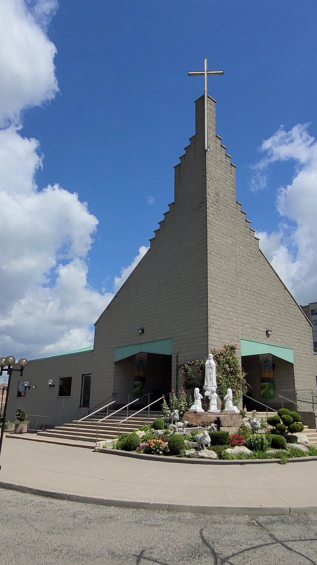 Our Lady of Fatima Church, a stone church whose stepped gable rises to a tall cross, with statues of the Fatima apparition among flower beds before the entrance
