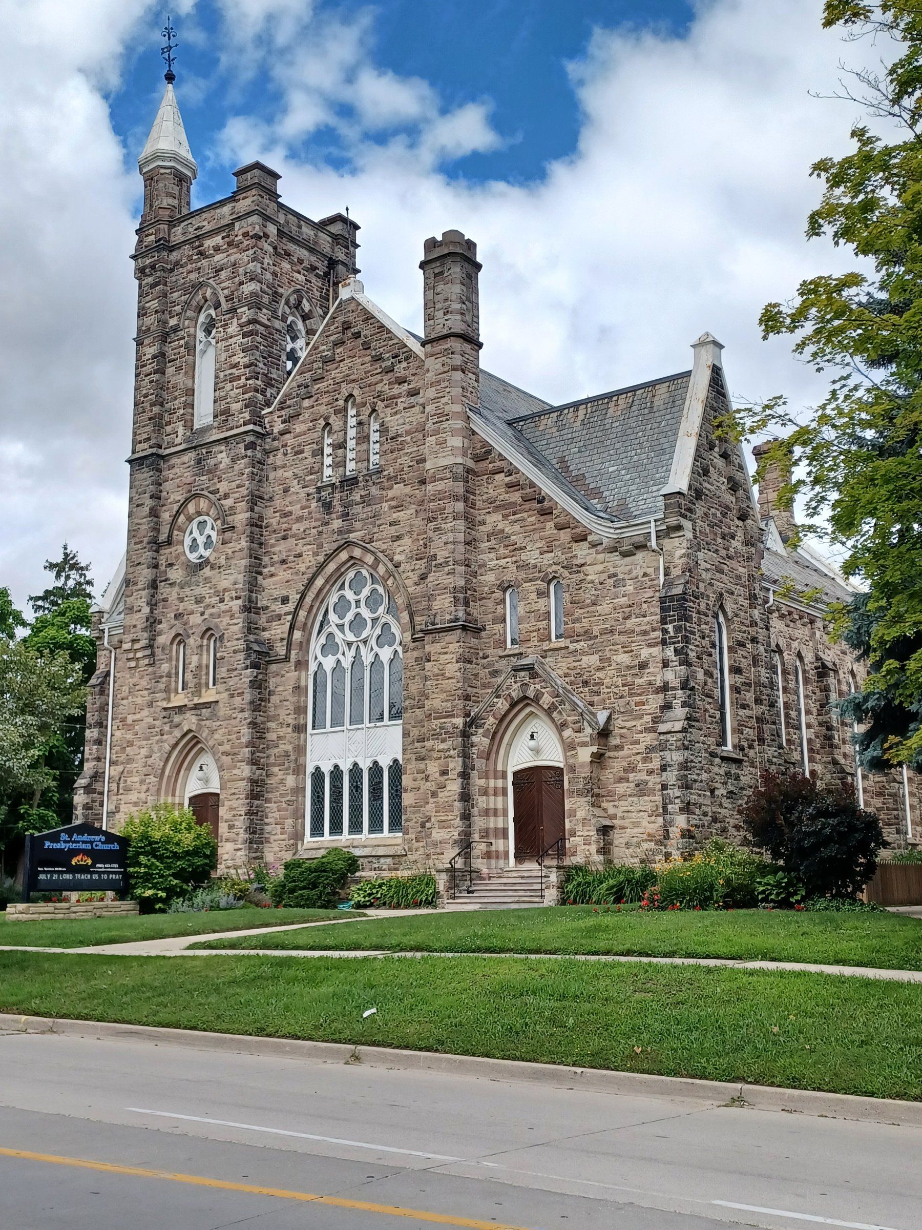 St. Andrew's Presbyterian Church, a Gothic church of rough-faced stone with a tall square steeple and a large traceried window, above a lawn