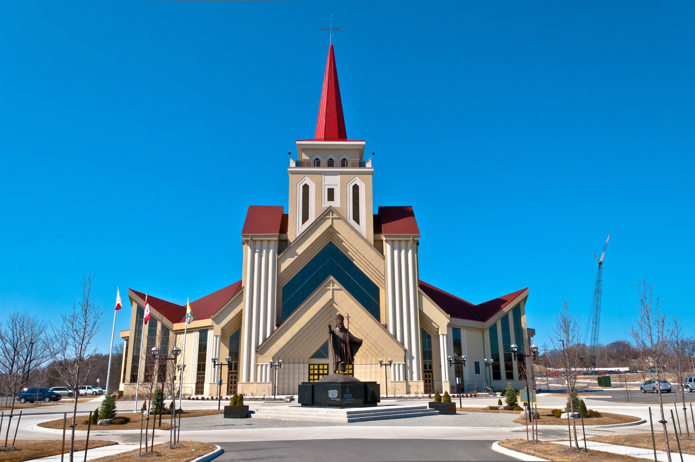 St. Eugene de Mazenod church, a modern building with a red spire rising from a pale tower and a bronze statue on a plinth before the entrance