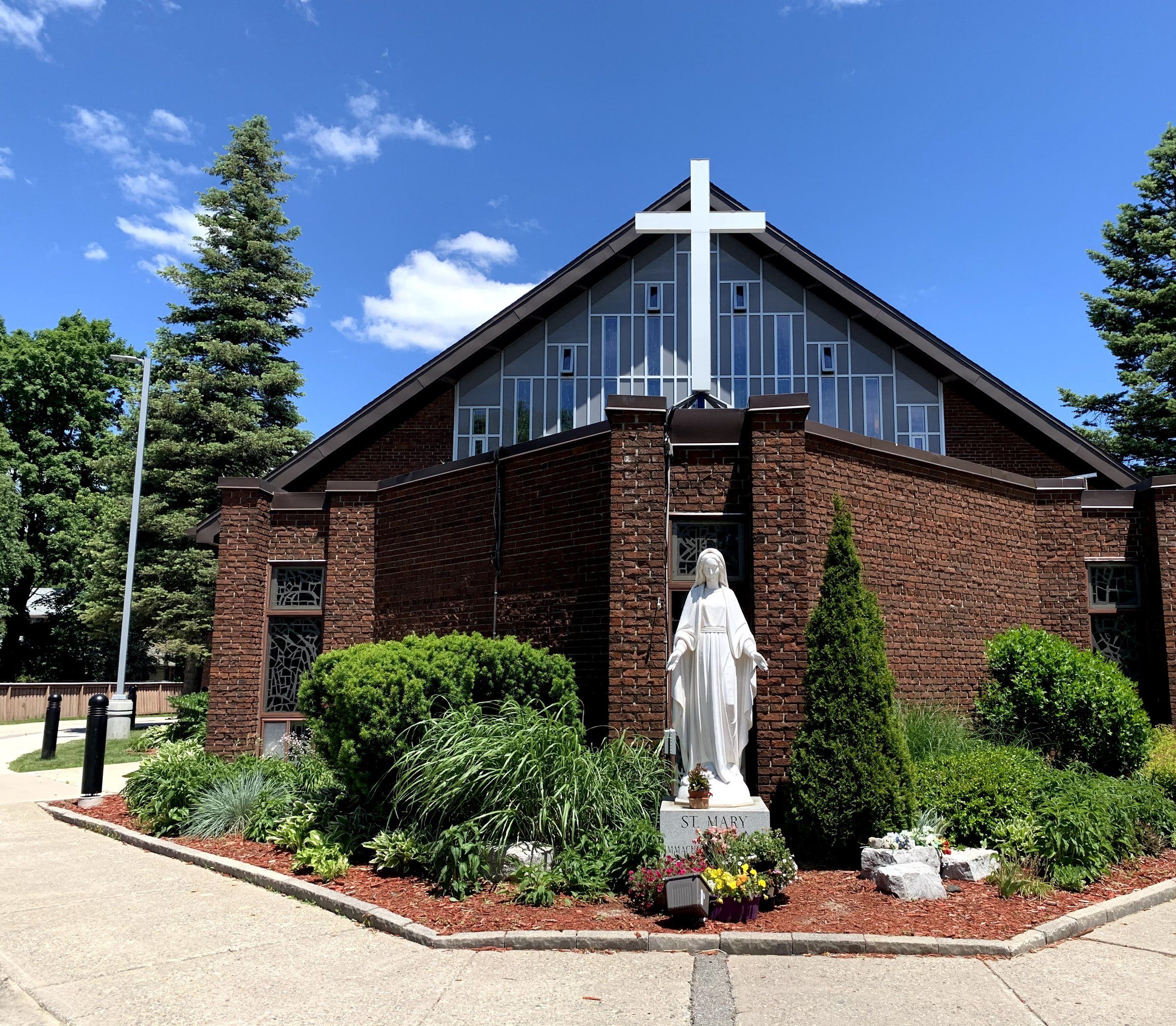 St. Mary's Catholic Church, a brick church whose glass gable carries a tall white cross, with a white statue of Mary in a flower bed in front