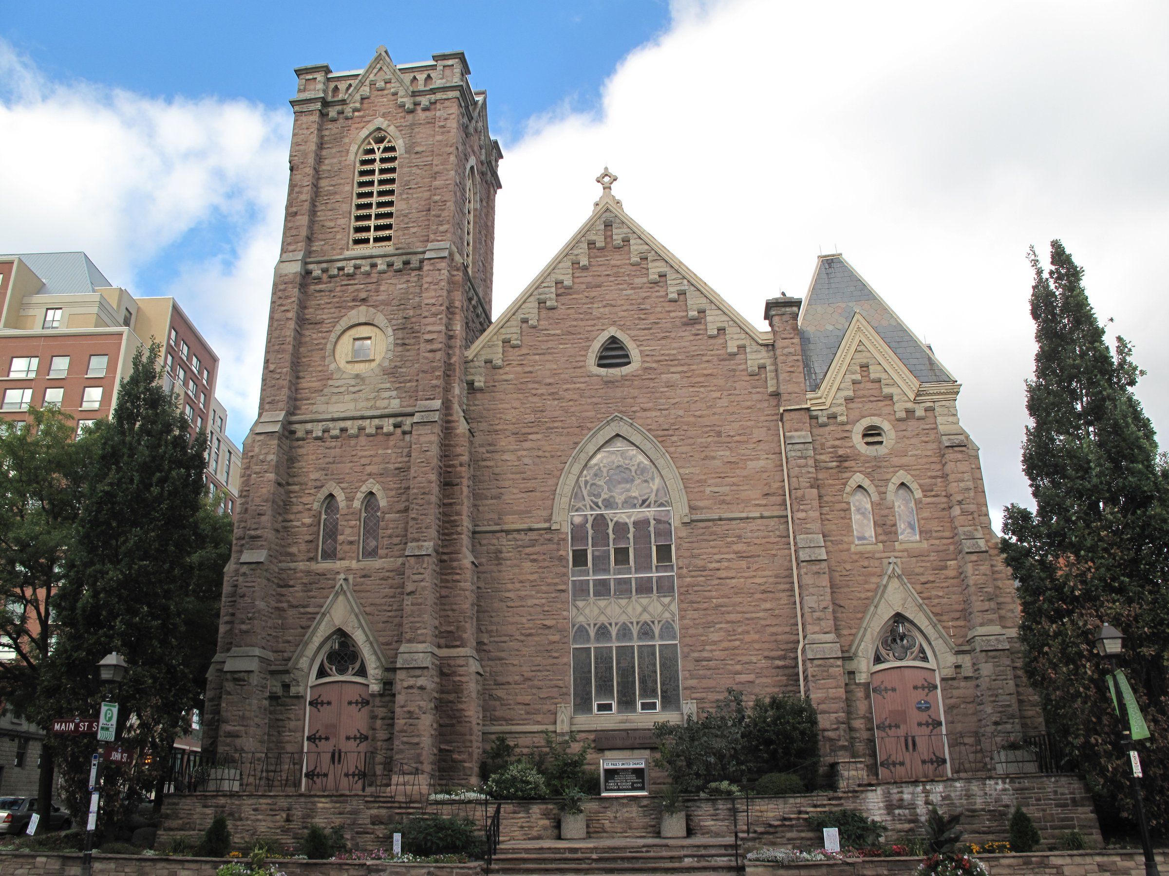 The brownstone front of St. Paul's United Church, with a square tower at its corner and a tall Gothic window between two arched doors